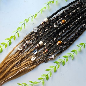 Pode incluir: Um conjunto de dreadlocks sintéticas castanhas e pretas com contas, conchas e pingentes. As dreadlocks são amarradas juntas com um fio de cobre.