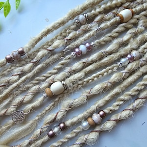 May include: Blonde synthetic dreadlocks with brown, white, and silver beads and charms. The dreadlocks are arranged in a row on a white surface.