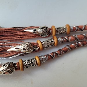 May include: Three strands of brown and silver braided hair extensions with decorative silver crow head charms and wooden beads.