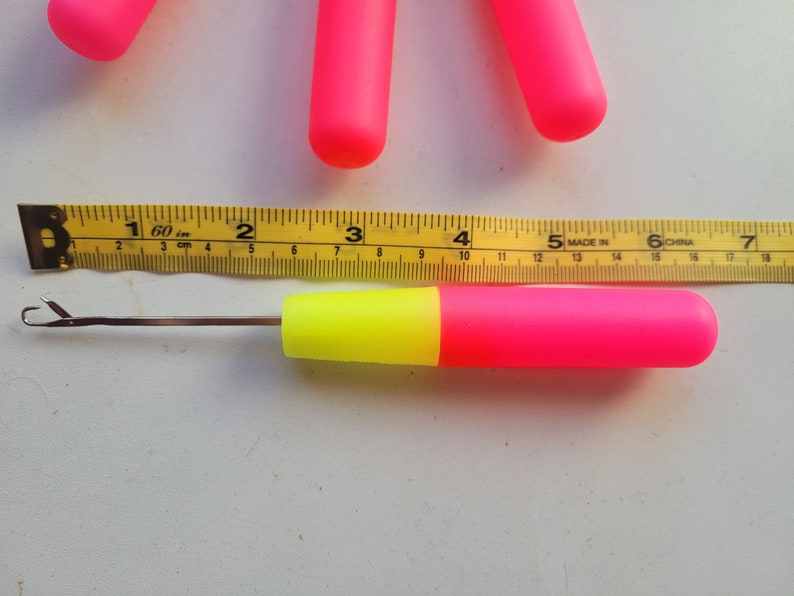 Peut inclure: Un crochet en plastique rose et jaune avec un crochet en m&eacute;tal. Le crochet mesure 12,7 cm de long et est mesur&eacute; &agrave; l'aide d'un m&egrave;tre ruban jaune.