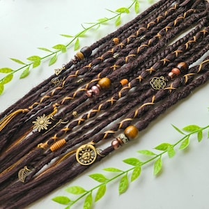 Puede incluir: Un conjunto de rastas sintéticas marrones con detalles dorados y marrones. Las rastas están decoradas con cuentas, abalorios y un cordón trenzado.