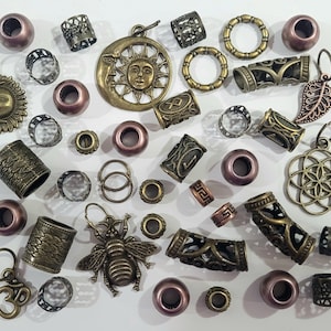 Puede incluir: Surtido de cuentas y abalorios para el pelo de metal en tonos bronce y dorado. Las cuentas son de diversas formas y tamaños, incluyendo redondas, cuadradas y cilíndricas. Algunas cuentas tienen diseños intrincados, mientras que otras son lisas. También hay varios abalorios, incluyendo un sol, una abeja y una flor.