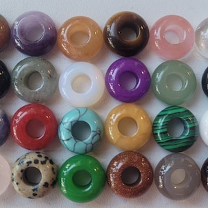 Puede incluir: Veinticuatro cuentas de piedras preciosas en forma de rosquilla en varios colores y patrones, incluidos rojo, verde, azul, morado, marrón, negro, blanco y rosa.