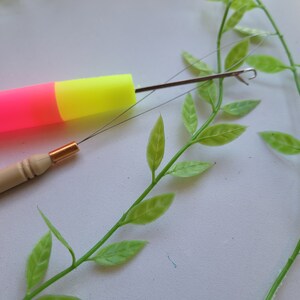 Peut inclure: Gros plan sur deux aiguilles &agrave; tricoter. L'une est une aiguille en plastique rose et jaune avec un crochet en m&eacute;tal. L'autre est une aiguille en bois avec une pointe en m&eacute;tal dor&eacute;.