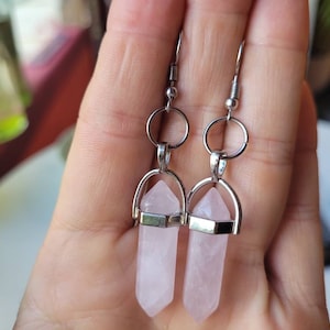 May include: A pair of silver earrings with pink crystal point pendants. The earrings are made of metal and have a simple design.