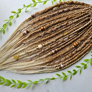 Könnte beinhalten: Ein Set aus blonden und braunen synthetischen Dreadlocks mit Perlen und goldenen Akzenten. Die Dreadlocks sind mit einem weißen Gummiband zusammengebunden.