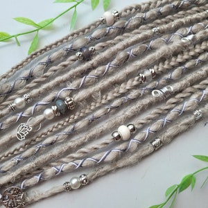 May include: A set of light brown synthetic dreadlocks with silver and white accents. The dreadlocks are decorated with silver beads, charms, and white string.