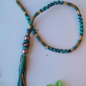 May include: A green, black, and gold braided cord with a tassel and brown beads. The cord is tied in a loop and has a black cord at the top.