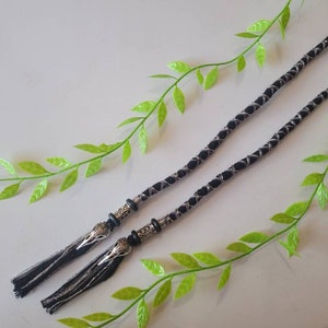 May include: Two black and silver braided cords with silver metal tassels. The cords have a decorative design and are tied together with a knot.