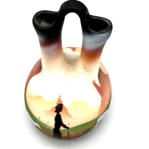 May include: A small, hand-painted ceramic vase with two spouts. The vase is decorated with a landscape scene in shades of brown, white, and green. A silhouette of a person is walking in the scene.
