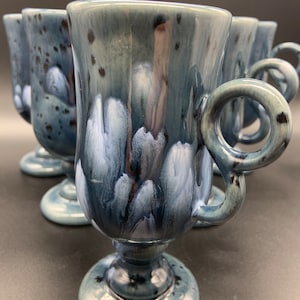 May include: Set of six blue and white ceramic mugs with a unique swirl design and a loop handle. The mugs have a footed base.