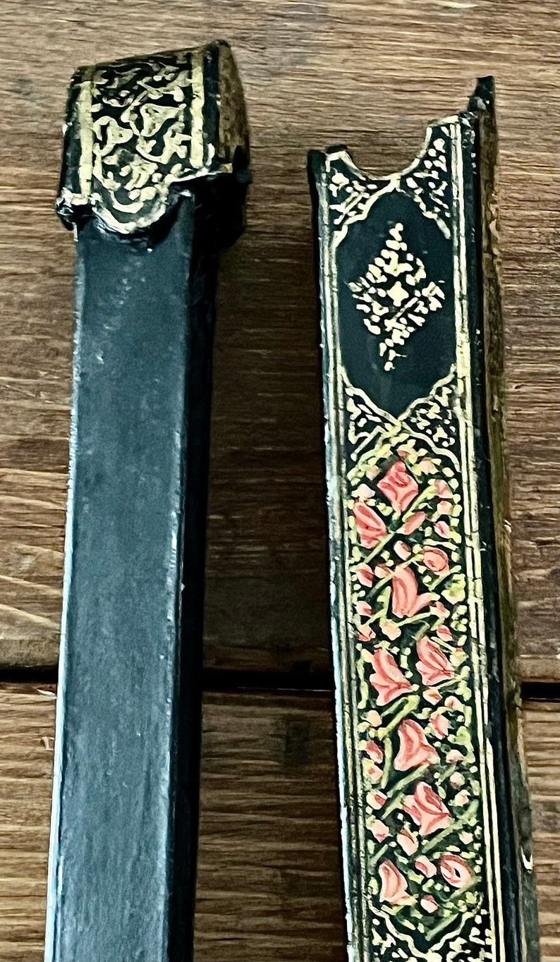 May include: Two black wooden boxes with intricate gold and red floral designs. The boxes are decorated with gold leaf and have a traditional, ornate style.