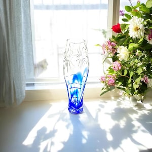 May include: A clear glass vase with a blue and white design. The vase is tall and slender with a round base. It is sitting on a white surface.