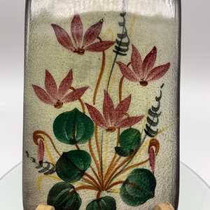May include: A rectangular ceramic dish with a floral design. The dish is painted with a white background and features pink flowers with green leaves and brown stems.