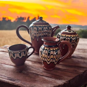 Op de afbeelding: Een set van vier bruine aardewerkstukken met zwarte en witte geometrische patronen. De set bevat een theepot, een kan, een suikerpot en een kop.