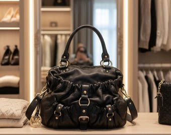 Bolso bandolera Michael Kors de piel granulada negra con herrajes dorados y bolsa guardapolvo.