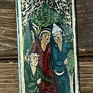 May include: A black wooden box with a gold trim and a painted scene of people in a garden. The box has a hinged lid and is decorated with floral patterns.