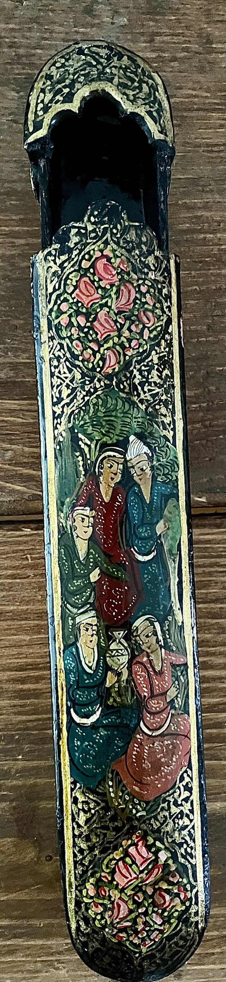 May include: A black wooden box with a gold trim and a painted scene of people in a garden. The box has a hinged lid and is decorated with floral patterns.