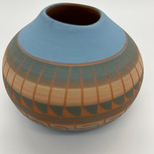 May include: A small, round, blue and brown pottery vase with a geometric design. The vase is hand-painted with a light blue glaze and has a brown and green geometric pattern.