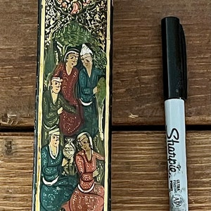 May include: A black and gold rectangular box with a floral design and a scene of people in traditional clothing. The box is decorated with intricate details and has a hinged lid.