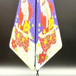 May include: Purple and white Christmas wind chime with a Santa Claus design. The chime features a purple triangle with a white snowflake design and a Santa Claus figure in a red suit with a white beard and a yellow trumpet. The chime also features a purple circle with a white house design.