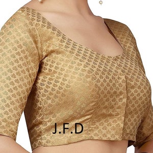 May include: A gold brocade blouse with a scoop neck and short sleeves. The blouse has a floral pattern and the text "J.F.D." is printed on the front.