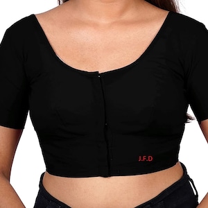 Puede incluir: Una blusa negra de manga corta con cierre de botón y el texto "J.F.D." bordado en la parte delantera.