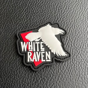 Puede incluir: Parche White Raven con una silueta blanca de un cuervo volando sobre un fondo rojo y negro.