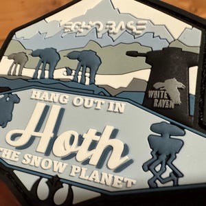 Puede incluir: Parche multicapa con temática de Star Wars. El diseño presenta el texto "Hang Out In Hoth The Snow Planet" y "Echo Base". El parche incluye imágenes de caminantes AT-AT, un paisaje nevado y un logotipo de White Raven.