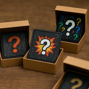 May include: Square black coasters with question mark designs in various colors, including orange, white, and blue, are displayed in small cardboard boxes. The coasters have a rubbery texture and a repeating question mark pattern.