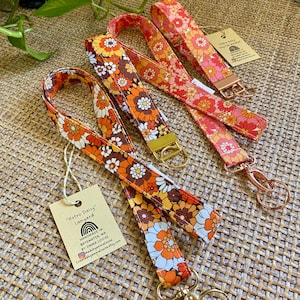May include: Three colourful retro daisy patterned fabric lanyards with gold key rings. The lanyards are handmade in Bayswater, WA by Emma Louise. The text "Retro Daisy" Lanyard is on a white tag.