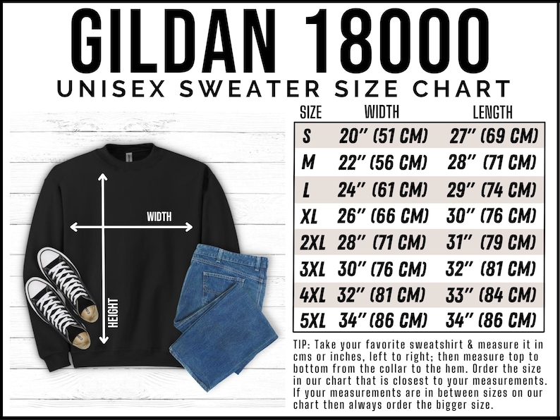 Op de afbeelding: Zwart Gildan 18000 unisex sweatshirt met een maattabel. De tabel geeft de maten S tot en met 5XL weer, met breedte- en lengtematen in inches en centimeters. De afbeelding bevat ook sneakers en een blauwe jeans.
