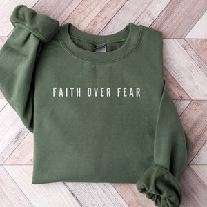 Puede incluir: Una sudadera verde con el texto "FAITH OVER FEAR" impreso en blanco en la parte delantera.