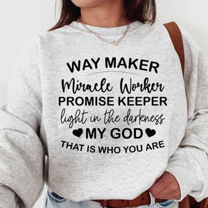 以下が含まれることがあります： 「WAY MAKER Miracle Worker PROMISE KEEPER light in the darkness MY GOD THAT IS WHO YOU ARE」という黒い文字がプリントされた、明るい灰色のスウェットシャツ。カジュアルなスタイル。