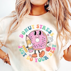 May include: A white t-shirt featuring a pink donut graphic and the text "Donut Stress Just Do Your Best". The donut has sprinkles and a smiling face. The text is in rainbow colours.