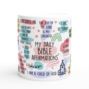 May include: White ceramic mug with colorful abstract shapes and stars. The mug features a variety of inspirational quotes, including "Jesus Loves Me", "The Joy of the Lord is My Strength", "I Am Victorious", "I Am a Child of God", and "My Daily Bible Affirmations".