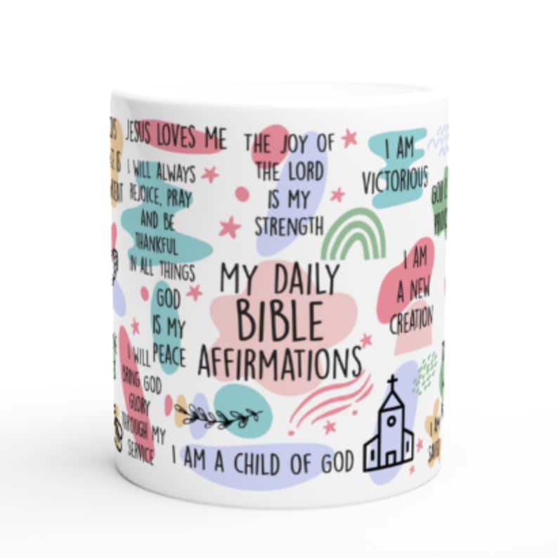 May include: White ceramic mug with colorful abstract shapes and stars. The mug features a variety of inspirational quotes, including "Jesus Loves Me", "The Joy of the Lord is My Strength", "I Am Victorious", "I Am a Child of God", and "My Daily Bible Affirmations".