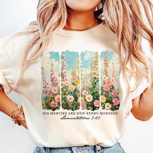 May include: A white t-shirt featuring a floral print and the text "His mercies are new every morning. Lamentations 3:23"