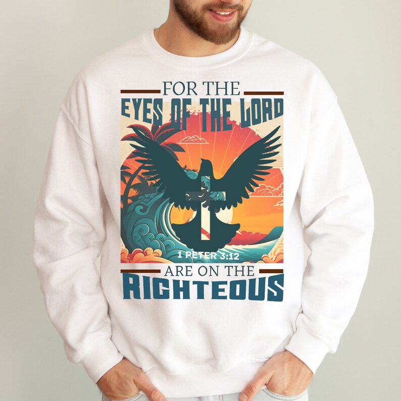 Puede incluir: Sudadera blanca con un dise&ntilde;o gr&aacute;fico que presenta una paloma volando sobre una cruz con una puesta de sol y una escena de oc&eacute;ano en el fondo. El texto dice "Porque los ojos del Se&ntilde;or est&aacute;n sobre los justos" y "1 Pedro 3:12".