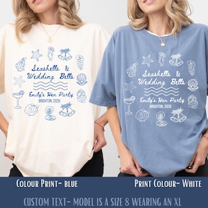 May include: Two t-shirts, one cream and one blue, with a graphic print of seashells, wedding bells, and the text "Seashells & Wedding Bells, Emily's Hen Party, Brighton, 2026." The print colours are blue and white.