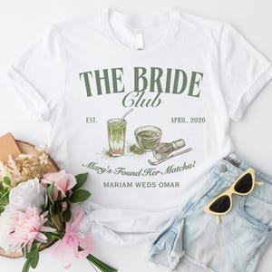 Może przedstawiać: Biała koszulka z napisem "THE BRIDE Club" w kolorze zielonym. Na koszulce znajdują się również słowa "EST. APRIL, 2026" oraz "Mary's Found Her Matcha! MARIAM WEDS OMAR" z ilustracją matcha.