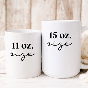 Op de afbeelding: Twee witte keramische mokken met zwarte tekst. De kleinere mok heeft de tekst "11 oz. size" en de grotere mok heeft de tekst "15 oz. size".