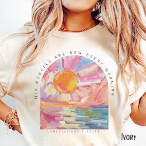 May include: A white t-shirt featuring a colourful sunrise graphic and the text "His mercies are new every morning" and "Lamentations 3:22-33". The shirt is labelled "Ivory".
