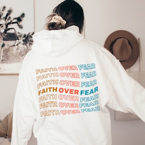 May include: White hoodie with the phrase "FAITH OVER FEAR" repeated in rainbow colors on the back.