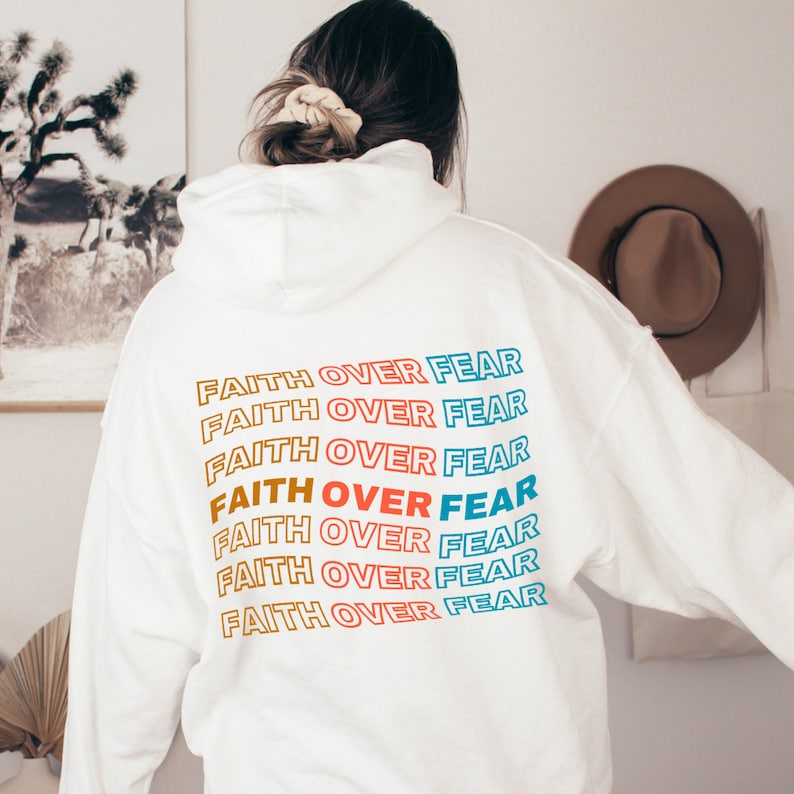 May include: White hoodie with the phrase "FAITH OVER FEAR" repeated in rainbow colors on the back.