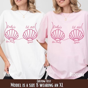 May include: Two t-shirts, one white and one pink, with a pink seashell design. The design includes the text "Emily's Hen Party Spain Est. 2025". The bottom of the image reads "Custom Text Model is a size 8 wearing an XL".