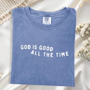 May include: A blue t-shirt with the text "GOD IS GOOD ALL THE TIME" in white lettering.