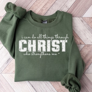Puede incluir: Una sudadera verde con el texto "i can do all things through CHRIST who strengthens me" en letras blancas desgastadas.