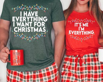 May include: Two Christmas-themed t-shirts, one military green and one red. The green shirt reads "I HAVE EVERYTHING I WANT FOR CHRISTMAS", the red shirt says "IT'S ME I'M EVERYTHING". Both have a Christmas lights design.