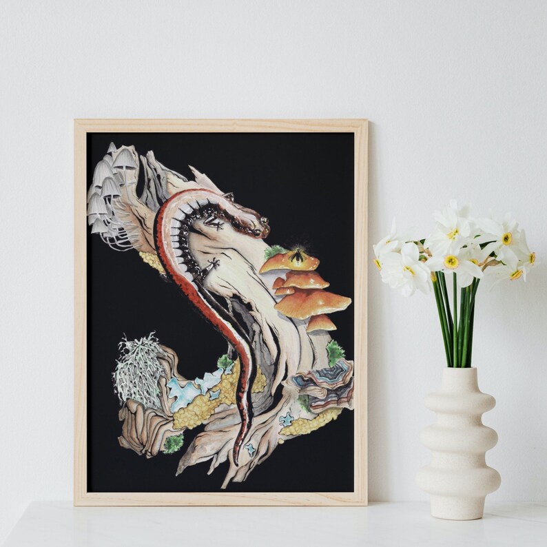 K&ouml;nnte beinhalten: Eine gerahmte Illustration einer Salamander, die sich um einen Ast mit Pilzen und wei&szlig;en Pilzen windet. Der Hintergrund ist schwarz und das Kunstwerk befindet sich in einem hellen Holzrahmen.